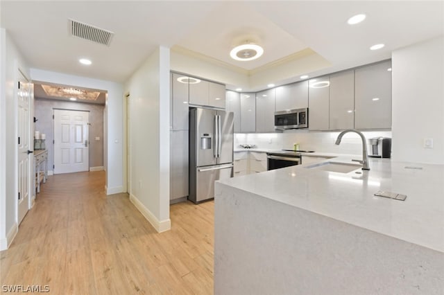 kitchen featuring sink, gray cabinetry, appliances with stainless steel finishes, light hardwood / wood-style flooring, and backsplash