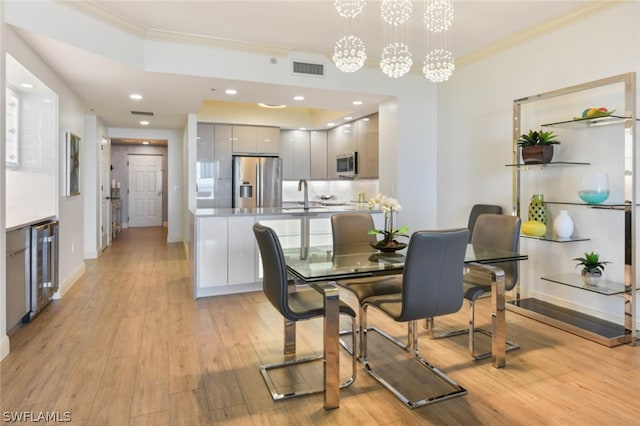 dining area featuring sink, crown molding, light hardwood / wood-style flooring, beverage cooler, and an inviting chandelier