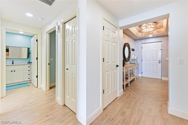 hall with light hardwood / wood-style floors, a chandelier, and a tray ceiling