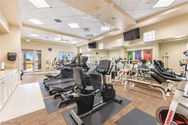 gym with ceiling fan, a drop ceiling, light colored carpet, and a high ceiling