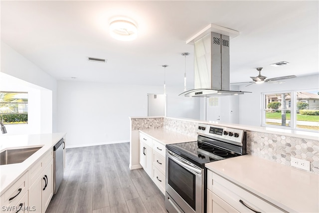 kitchen with island range hood, stainless steel appliances, ceiling fan, tasteful backsplash, and white cabinetry