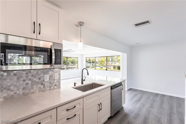 kitchen with stainless steel appliances, hardwood / wood-style floors, white cabinets, hanging light fixtures, and sink