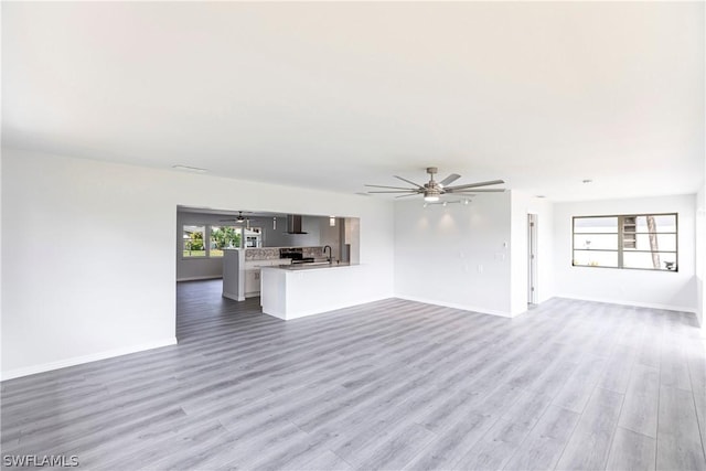 unfurnished living room featuring baseboards, light wood-style flooring, a sink, and ceiling fan