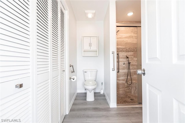 full bathroom featuring toilet, baseboards, a shower stall, a closet, and wood finished floors