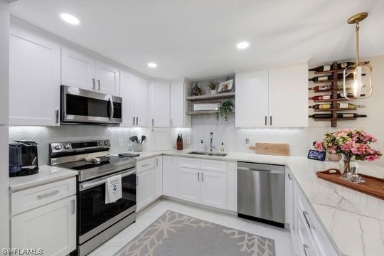 kitchen featuring light stone countertops, tasteful backsplash, appliances with stainless steel finishes, white cabinets, and sink