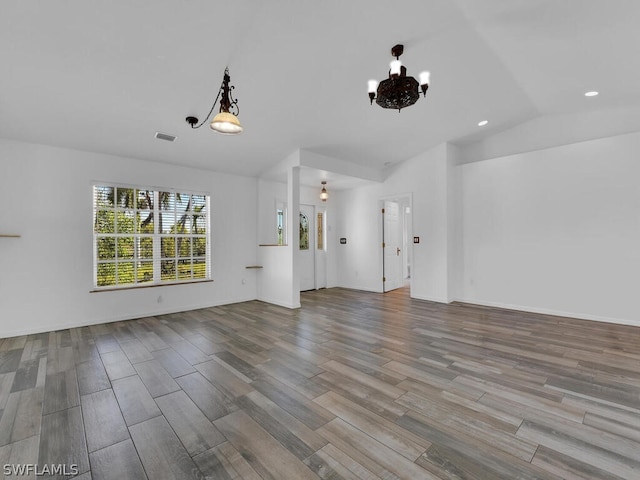 unfurnished living room featuring an inviting chandelier, light hardwood / wood-style flooring, and vaulted ceiling