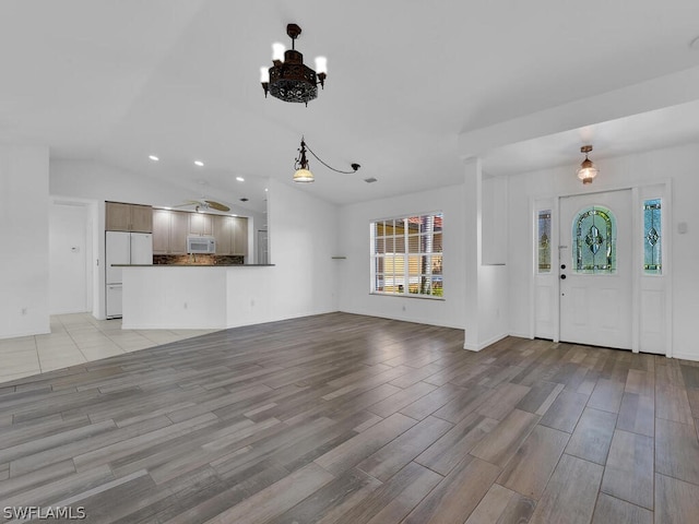 unfurnished living room featuring ceiling fan with notable chandelier, vaulted ceiling, and light hardwood / wood-style floors