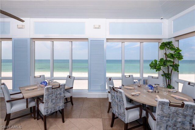 tiled dining room with a water view, a healthy amount of sunlight, and a view of the beach