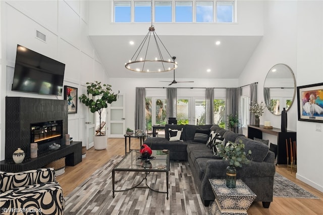 living room with ceiling fan with notable chandelier, light hardwood / wood-style flooring, and high vaulted ceiling