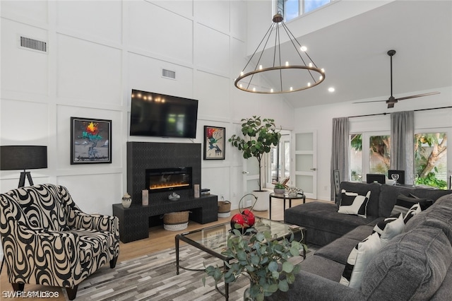 living room with a high ceiling, ceiling fan with notable chandelier, hardwood / wood-style flooring, and a healthy amount of sunlight