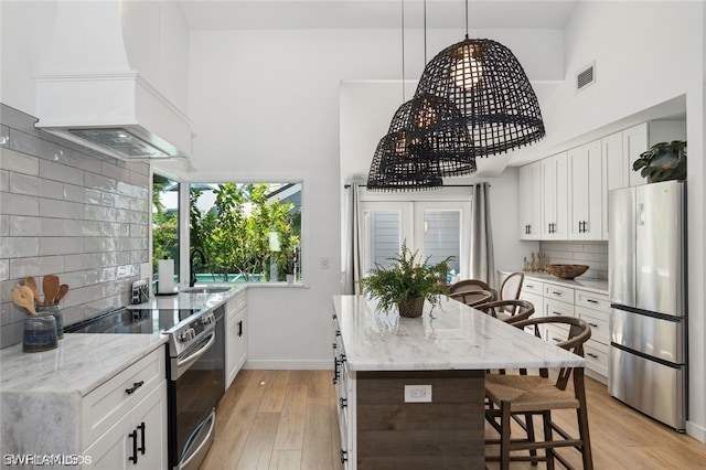 kitchen featuring white cabinets, premium range hood, stainless steel appliances, and light hardwood / wood-style flooring