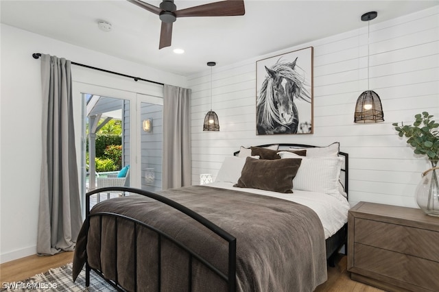 bedroom with access to exterior, light hardwood / wood-style floors, ceiling fan, and wooden walls