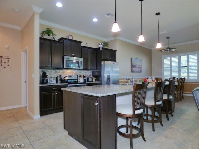 kitchen featuring appliances with stainless steel finishes, a center island with sink, decorative light fixtures, and ornamental molding