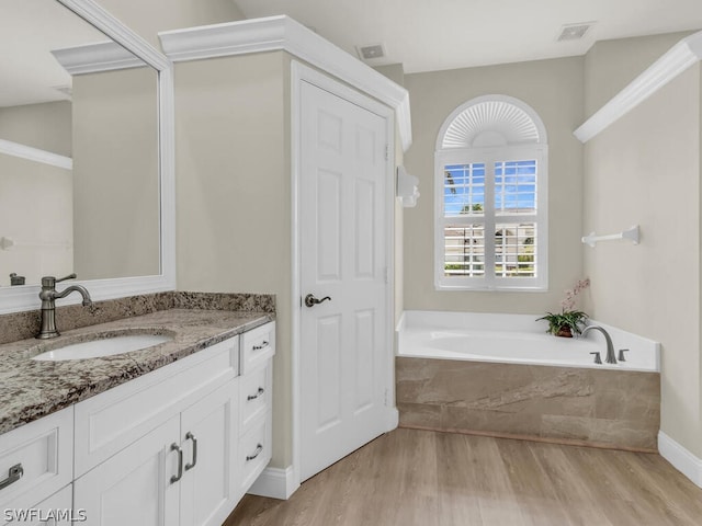 bathroom with hardwood / wood-style flooring, a relaxing tiled tub, and vanity