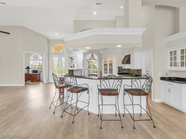 kitchen featuring french doors, backsplash, wall chimney exhaust hood, white cabinetry, and hanging light fixtures