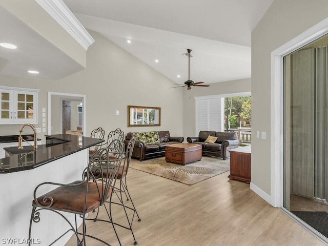 interior space featuring a breakfast bar, lofted ceiling, white cabinets, light hardwood / wood-style flooring, and ceiling fan