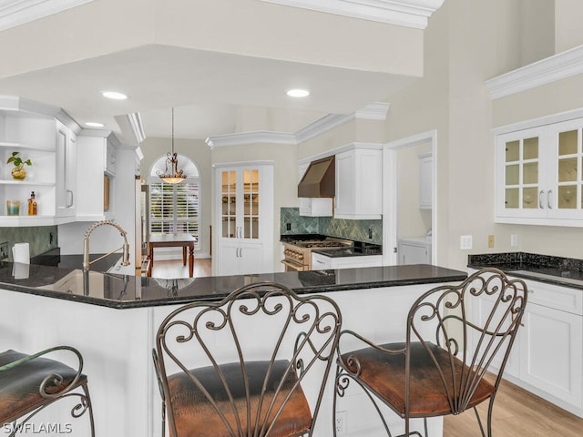 kitchen with premium range hood, kitchen peninsula, decorative light fixtures, a kitchen bar, and white cabinetry