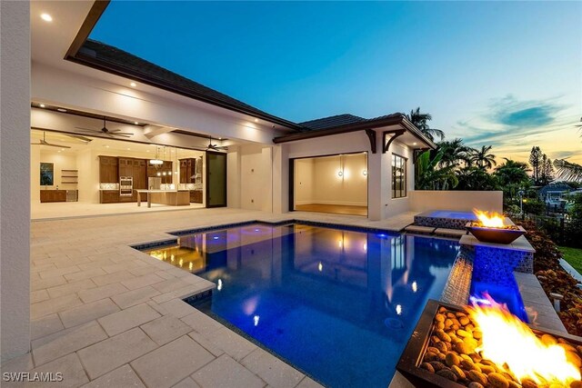 pool at dusk featuring a fire pit, ceiling fan, a hot tub, and a patio area