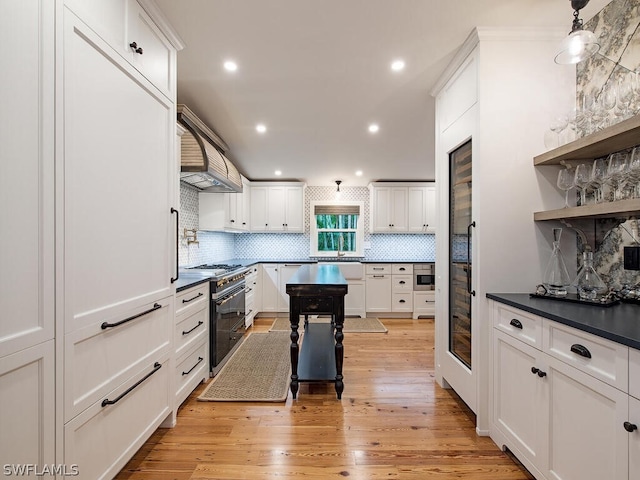 kitchen featuring range with two ovens, custom exhaust hood, backsplash, and light hardwood / wood-style flooring