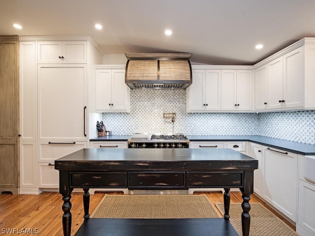 kitchen with white cabinets, tasteful backsplash, light wood-type flooring, and wall chimney range hood