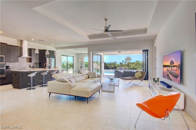 living room with ceiling fan, light tile patterned flooring, a raised ceiling, and sink