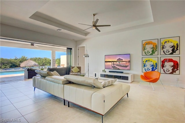 living room with a raised ceiling, ceiling fan, and light tile patterned floors