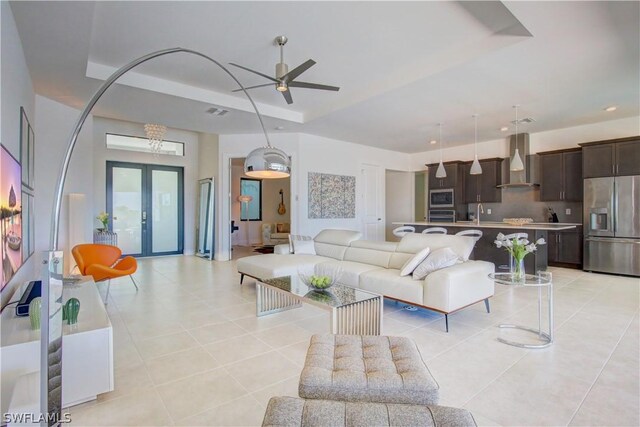 tiled living room with ceiling fan, french doors, a raised ceiling, and sink