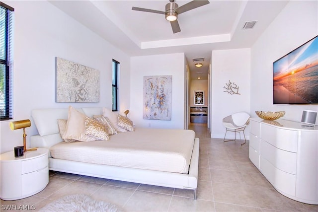 bedroom with ceiling fan, a tray ceiling, and light tile patterned floors