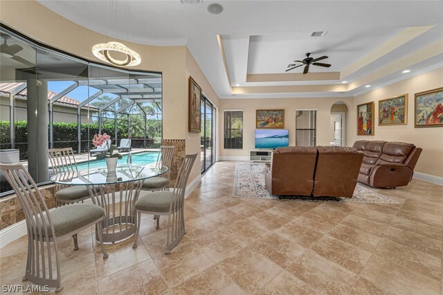 tiled living room featuring a raised ceiling, ornamental molding, and ceiling fan with notable chandelier