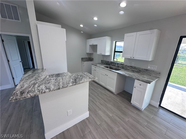 kitchen with light hardwood / wood-style floors, white cabinets, light stone counters, and sink