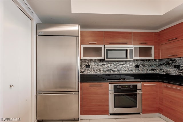 kitchen featuring appliances with stainless steel finishes, backsplash, light tile flooring, and dark stone counters