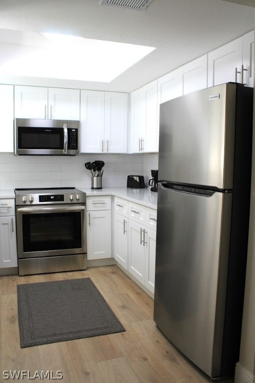 kitchen with backsplash, light hardwood / wood-style floors, white cabinets, and appliances with stainless steel finishes