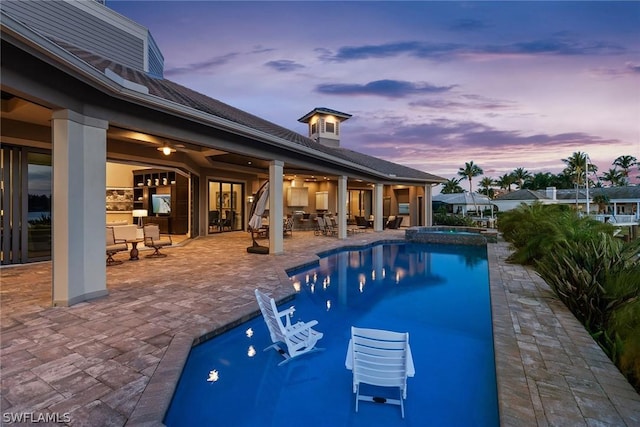 pool at dusk with an in ground hot tub and a patio