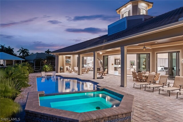 pool at dusk featuring a patio, ceiling fan, and an in ground hot tub