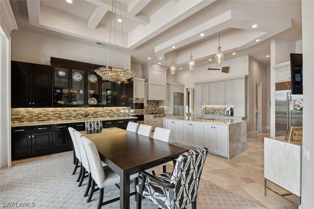 tiled dining space featuring an inviting chandelier, sink, a raised ceiling, and a high ceiling