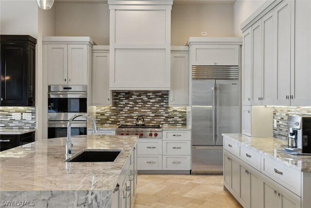 kitchen with sink, stainless steel appliances, backsplash, and light stone counters