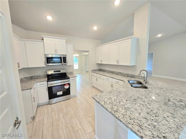 kitchen with light stone countertops, a peninsula, a sink, stainless steel appliances, and white cabinetry