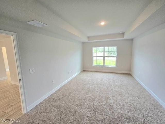 spare room featuring visible vents, light colored carpet, a raised ceiling, and baseboards