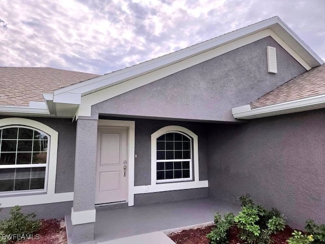 view of exterior entry with roof with shingles and stucco siding