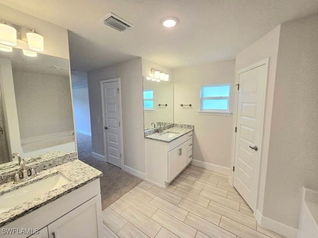 full bath with a sink, visible vents, two vanities, and a bath