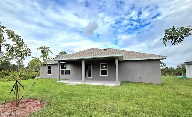 rear view of property with stucco siding, a patio, a lawn, and roof with shingles