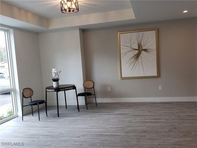 living area with light hardwood / wood-style floors, a raised ceiling, and an inviting chandelier