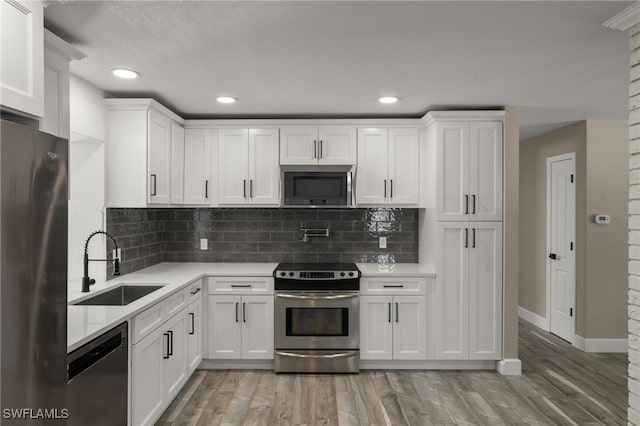 kitchen with wood-type flooring, appliances with stainless steel finishes, tasteful backsplash, sink, and white cabinets