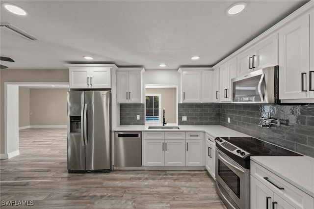 kitchen with appliances with stainless steel finishes, white cabinetry, sink, and light hardwood / wood-style floors