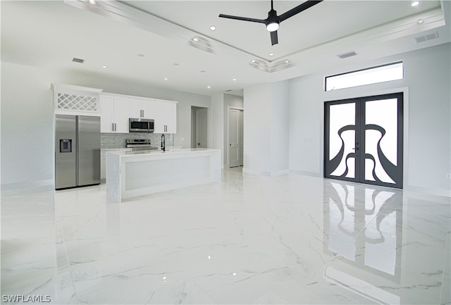 kitchen featuring appliances with stainless steel finishes, white cabinets, light tile flooring, tasteful backsplash, and a center island with sink