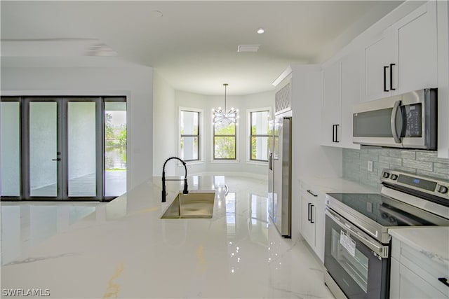 kitchen with decorative light fixtures, stainless steel appliances, tasteful backsplash, white cabinetry, and a chandelier