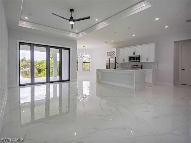 kitchen with a kitchen island with sink, stainless steel appliances, light tile floors, and a raised ceiling