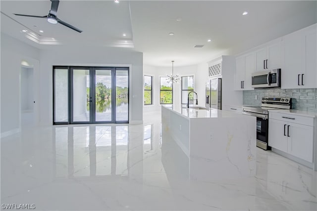 kitchen with white cabinets, an island with sink, light tile floors, and stainless steel appliances