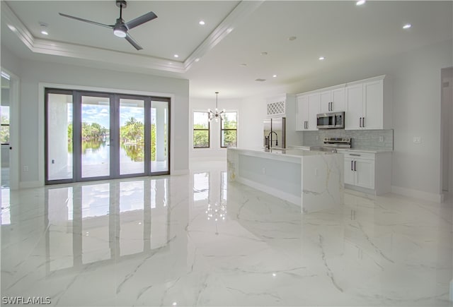 kitchen with appliances with stainless steel finishes, light tile flooring, a raised ceiling, and a kitchen island with sink