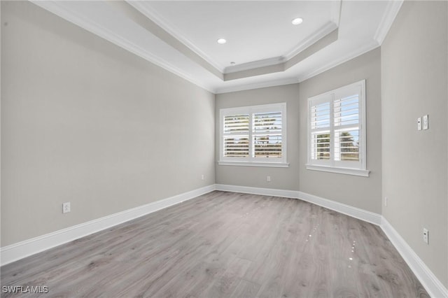 unfurnished room featuring light wood finished floors, baseboards, ornamental molding, and a raised ceiling